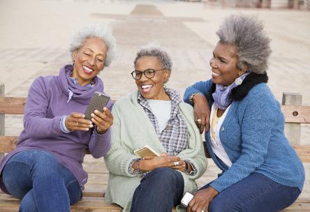 Three older woman sitting on a park bench laughing